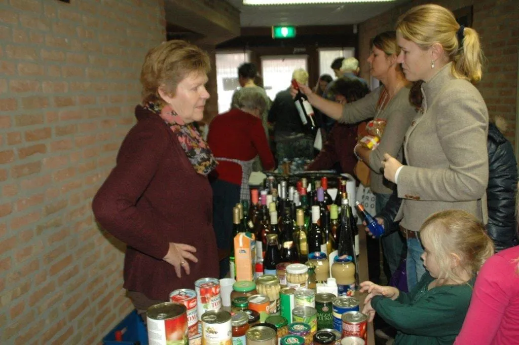 Bezoekers bij een kraam met flessen en boeken op de bazaar.