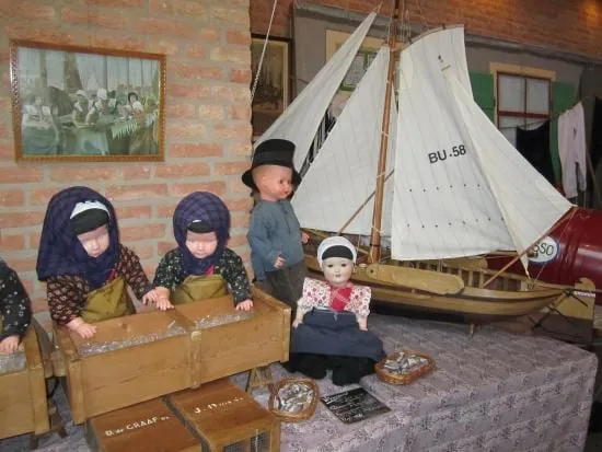 Kinderpoppen bij een miniatuurbotter met bruin zeil.