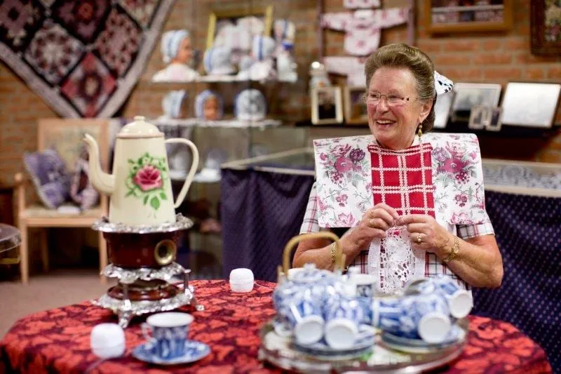 Pop met rode geruite kraplap aan een theetafel met Delfts blauw.
