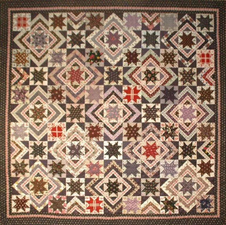 Quilt met sterrenblokken in rood, blauw en zand.