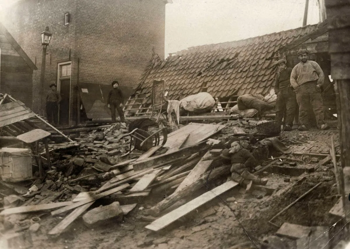 Historische foto van de watersnood van 1916: vrouwen in dracht voor een huis in het ondergelopen dorp.
