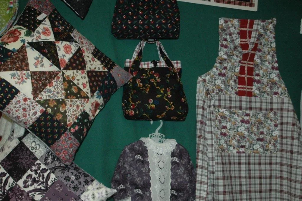 Stapels lapjes klederdrachtstof en quiltblokken op een tafel in het winkeltje.